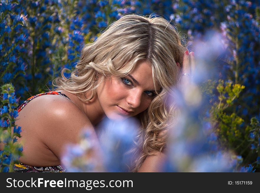 Portrait of a blue-eyed blonde young woman on a background of blue wild flowers. summer, outdoors.