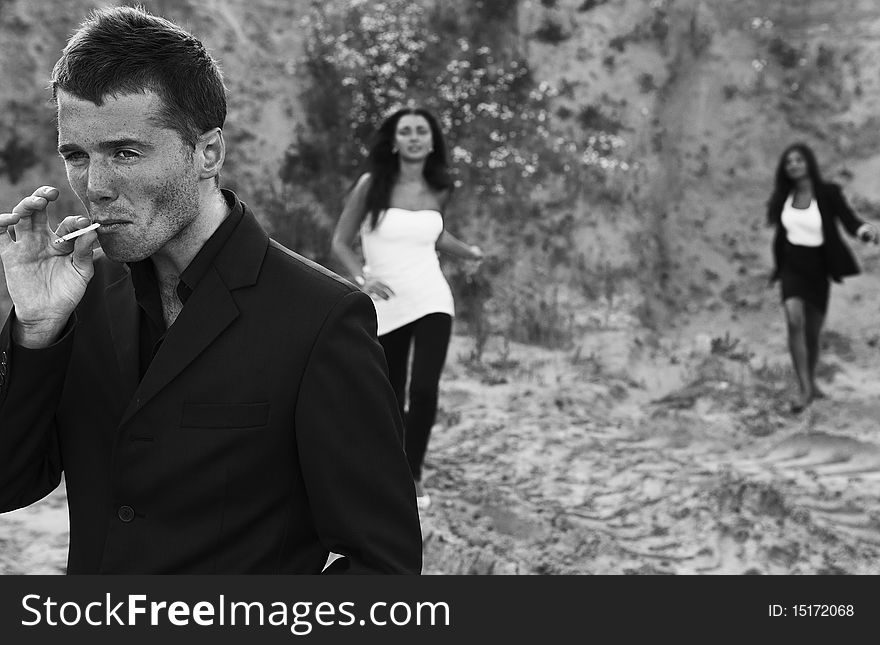 Smoking macho in an elegant suit and two girls behind his back. Photo.