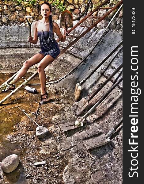 Attractive woman in a stone hole among old shovels. HDR style Photo.