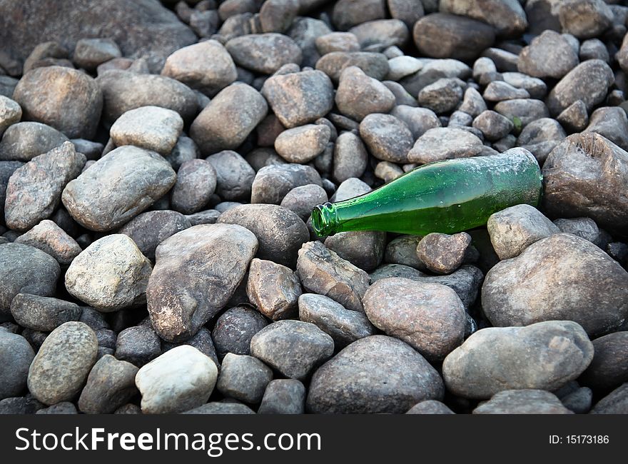 A green bottle on a rock bed by a lake. A green bottle on a rock bed by a lake