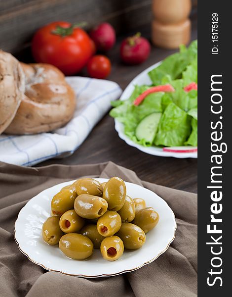 Close up of green olives in small plate with some other food on the background. Close up of green olives in small plate with some other food on the background