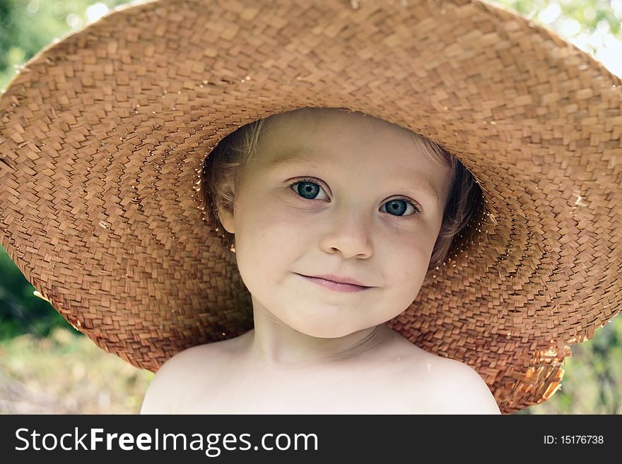 Little cheerful girl in big old straw hat