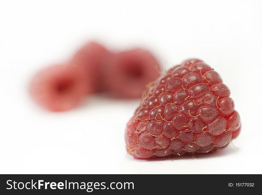 Closeup on a rasperry against a white background with more berries blurred behind. Closeup on a rasperry against a white background with more berries blurred behind.