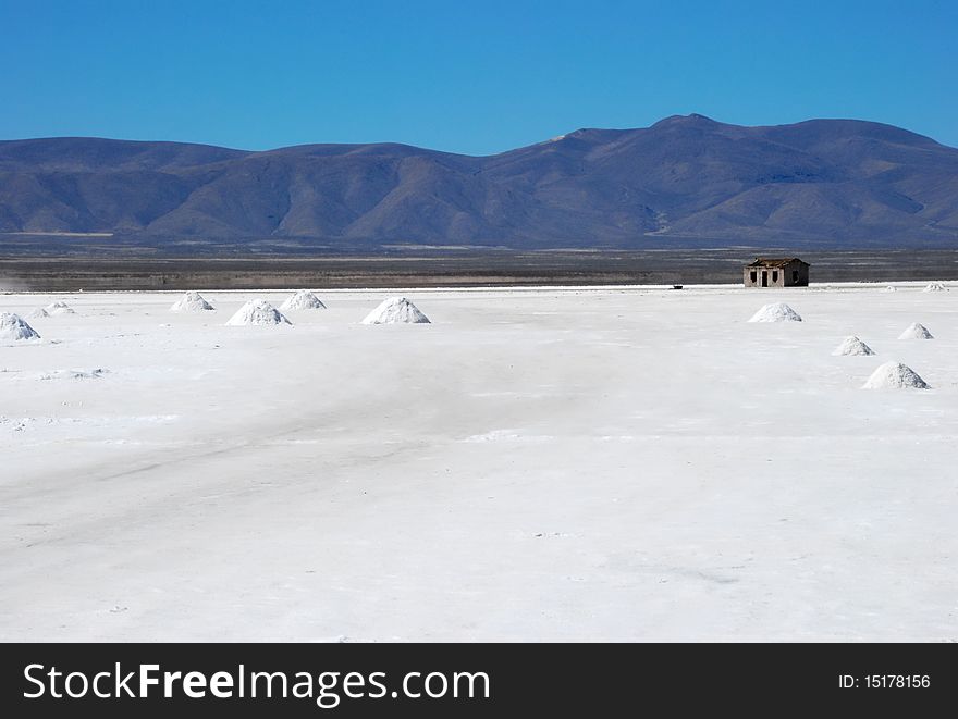 Lonely house in salt desert with salt piles and mountains.