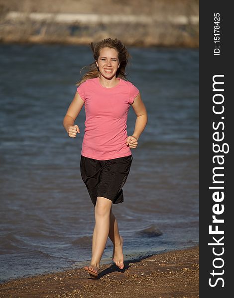 A young teenager in a pink shirt and black shorts running barefoot on the beach. A young teenager in a pink shirt and black shorts running barefoot on the beach.