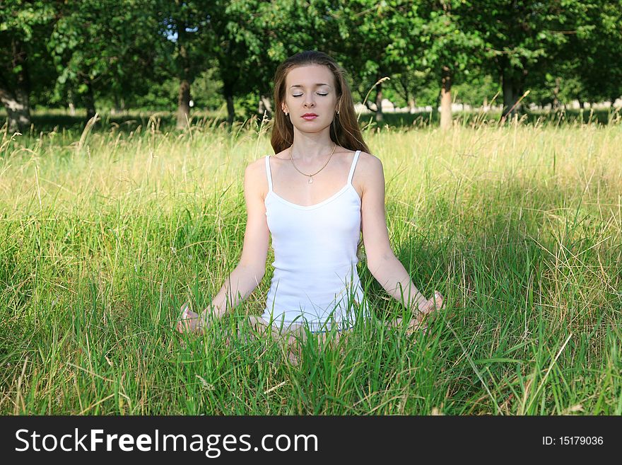Beautiful young girl in white, sitting on the grass and meditate on the background of green trees. Beautiful young girl in white, sitting on the grass and meditate on the background of green trees