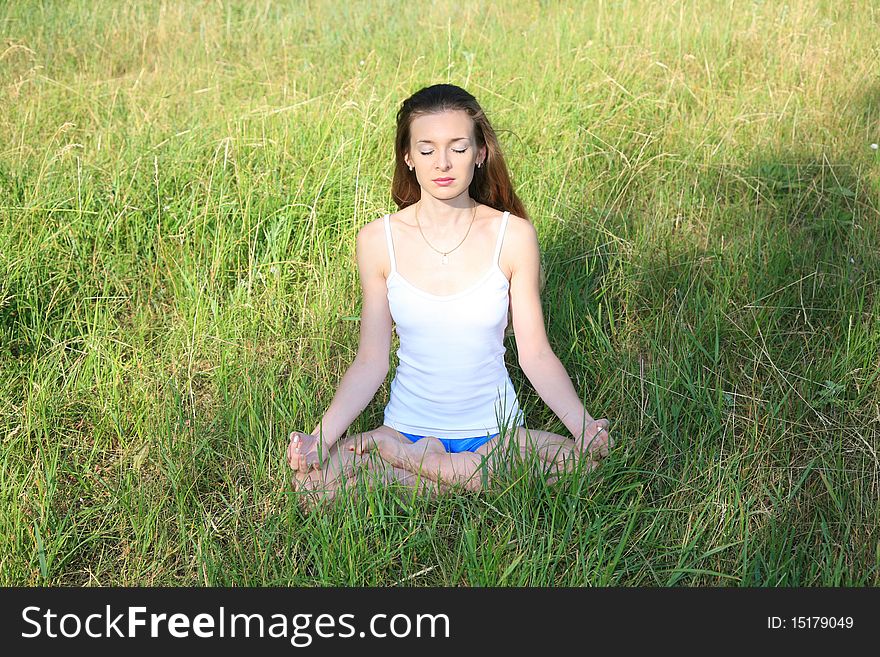 Beautiful young girl sitting with her eyes closed in the green grass and meditating, enjoying the sun. Beautiful young girl sitting with her eyes closed in the green grass and meditating, enjoying the sun