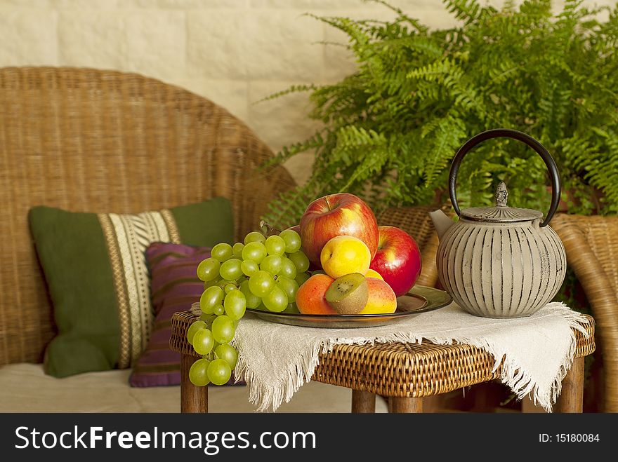 Beautiful still life image of fruits and teapot in the interior with wicker furniture