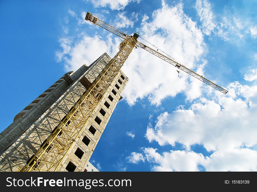 Photos of high-rise construction cranes and unfinished house against the blue sky with clouds. Taken from the bottom up