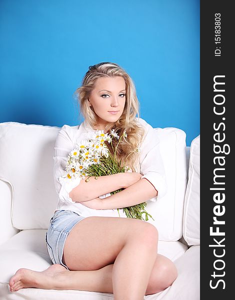 Beautiful girl with a bouquet of camomiles sits on a sofa