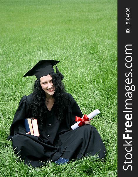 Happy bachelor with diploma sitting on the grass