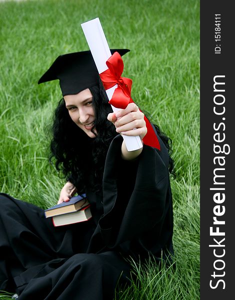 Smiling caucasian student with diploma sitting on the grass