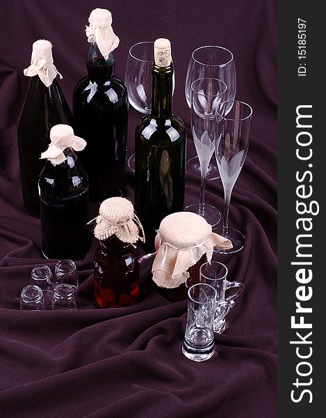 Bottles and empty glasses on a dark background, suggest homemade liquor and juice, four kind of empty glasses. Bottles and empty glasses on a dark background, suggest homemade liquor and juice, four kind of empty glasses.