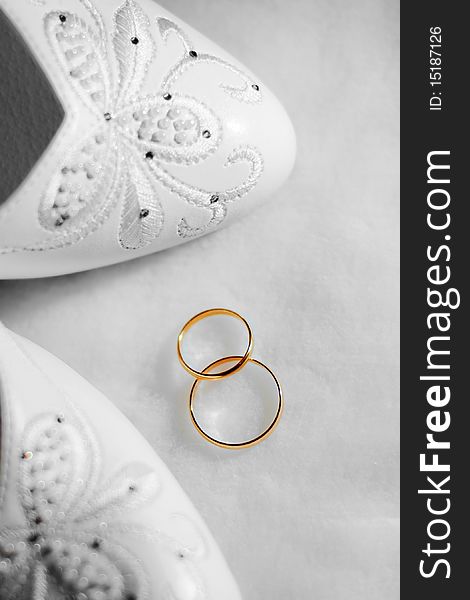 Two gold wedding rings and shoes on white background
