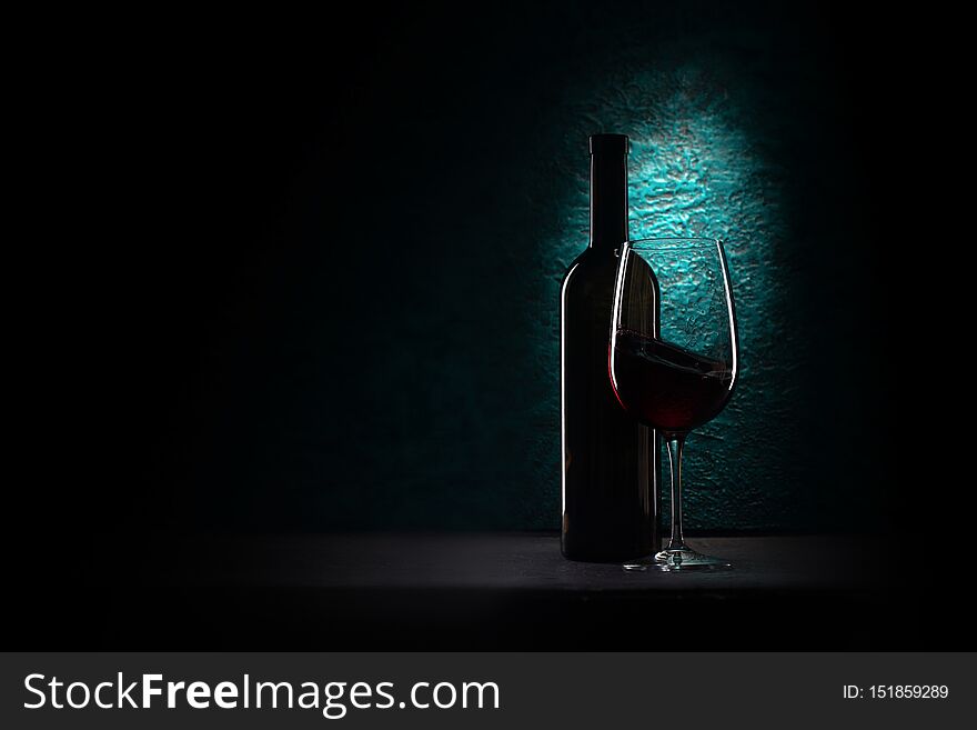 Glass of red wine and bottle on azure stone background, drink against the wall in the old cellar