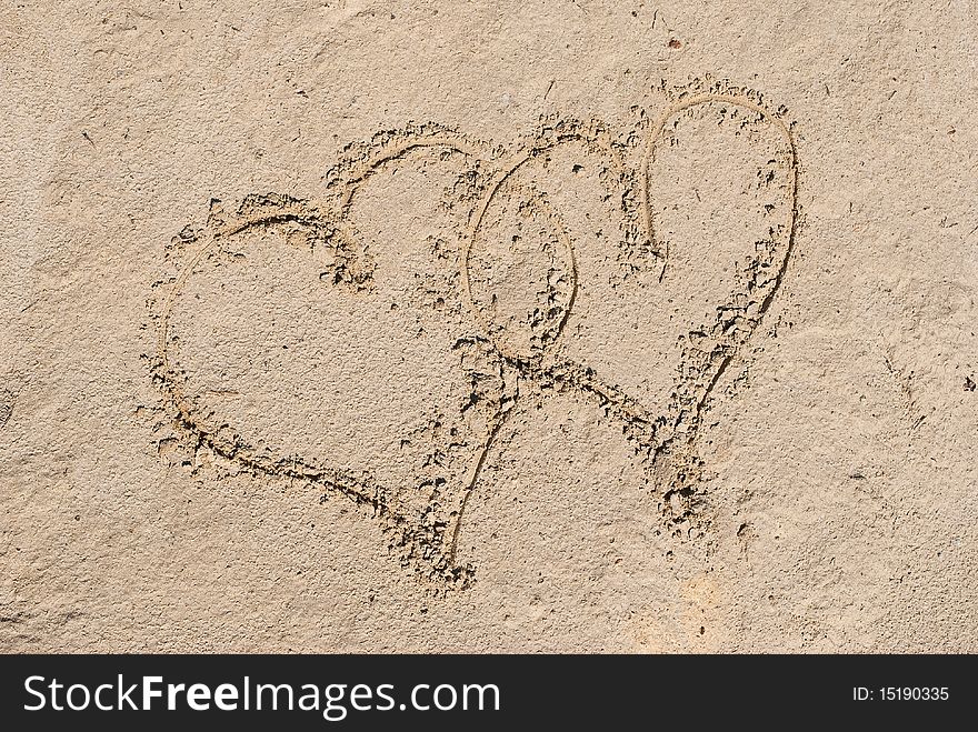 Two entangled hearts drawn out on a sandy beach