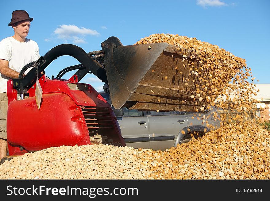 Man operating small earth moving machine on gravel