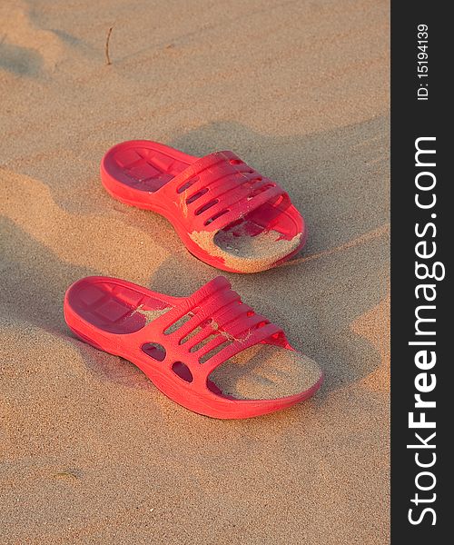 Red rubber beach shoes on the sand background. Red rubber beach shoes on the sand background