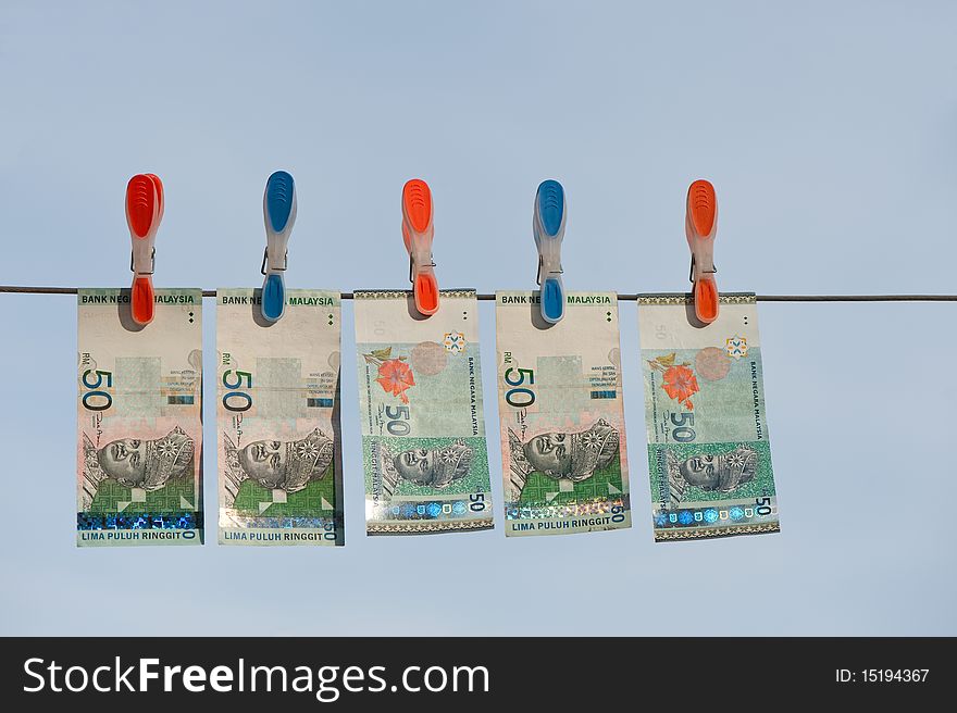 Five drying ringgit bills on a line