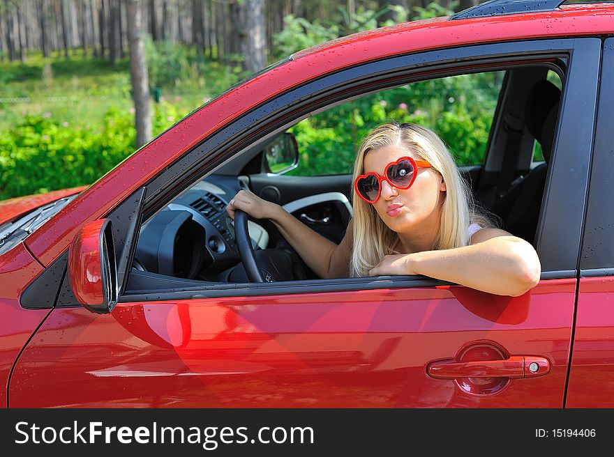 Beautiful funny woman in heart shaped glasses in red shiny car outdoors. Beautiful funny woman in heart shaped glasses in red shiny car outdoors