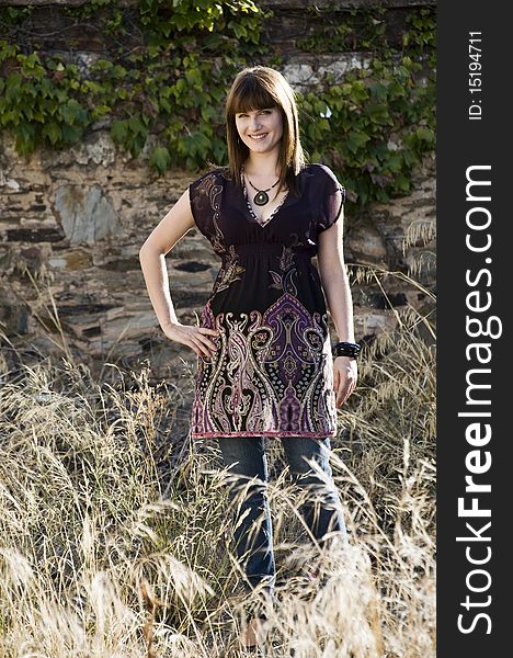 Beautiful woman stands in the afternoon light by a stone wall. Beautiful woman stands in the afternoon light by a stone wall.