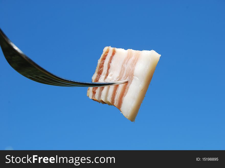 A fork with a slice of bacon is silhouetted against a blue sky