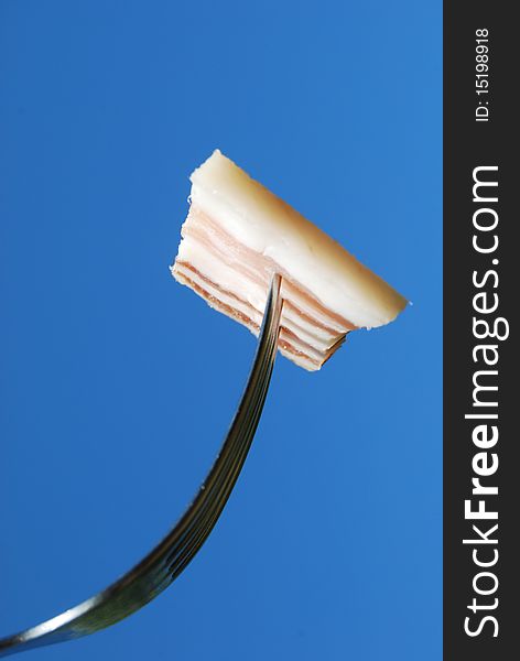 A fork with a slice of bacon is silhouetted against a blue sky