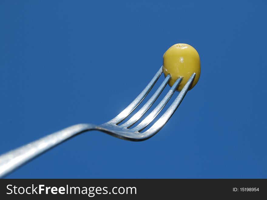 A fork with an olive green stands out against a blue sky. A fork with an olive green stands out against a blue sky