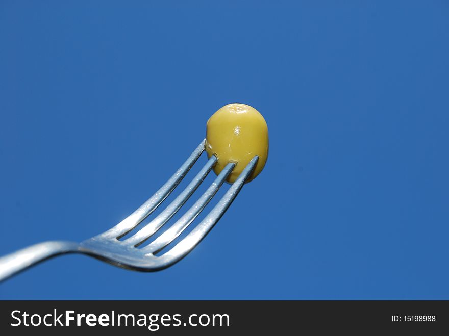 A fork with a green olive is silhouetted against a blue sky. A fork with a green olive is silhouetted against a blue sky