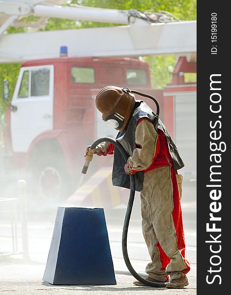 Worker in a protective suit spraying sand with abrasive peeler
