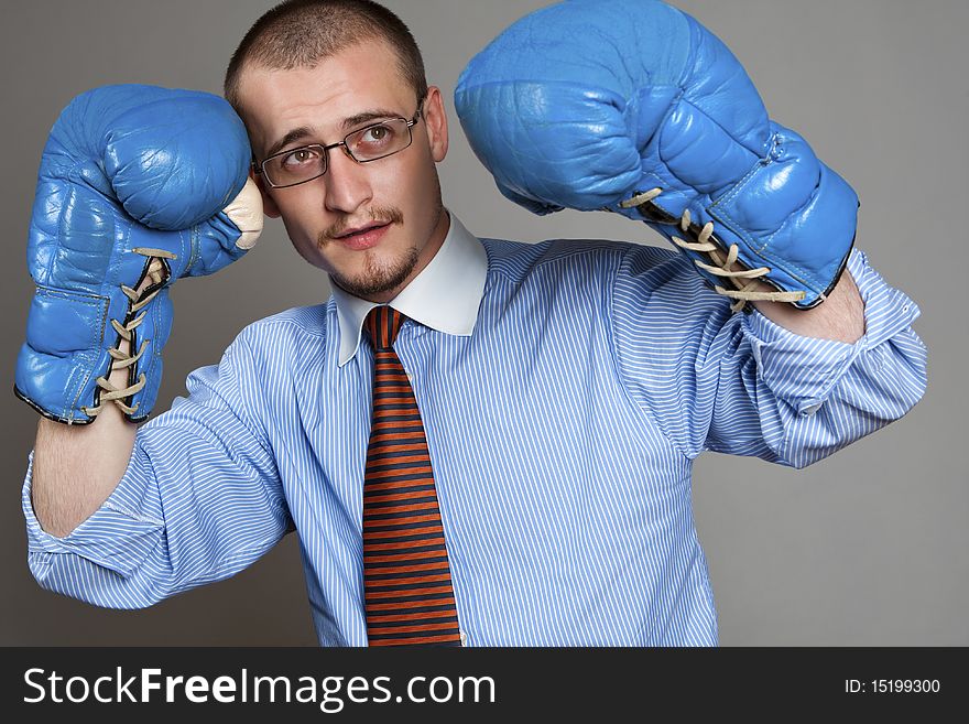 Young businessman wearing blue boxing-gloves isolated on gray