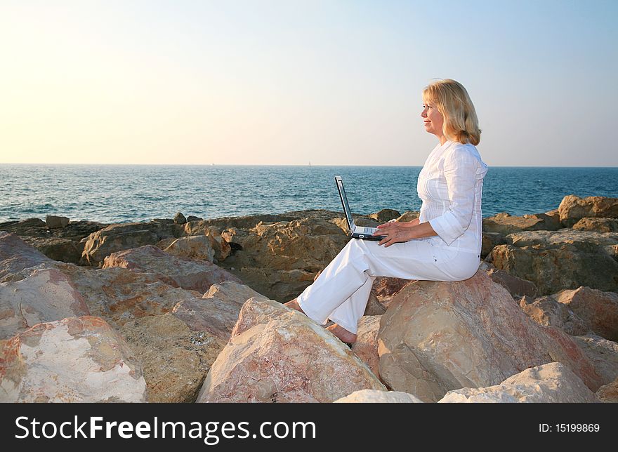 Beautiful blond woman sitting with a laptop on the background of the sea. Beautiful blond woman sitting with a laptop on the background of the sea