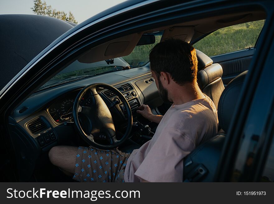 The guy in the pink t-shirt checks the engine of a black car lifting the hood in the country outside the road. The guy in the pink t-shirt checks the engine of a black car lifting the hood in the country outside the road