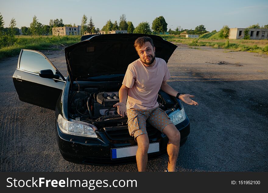 A Young Man Repairs A Car At Sunset Outside The City