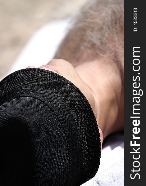 Man sunbathing on the beach with black fedora hat. Man sunbathing on the beach with black fedora hat