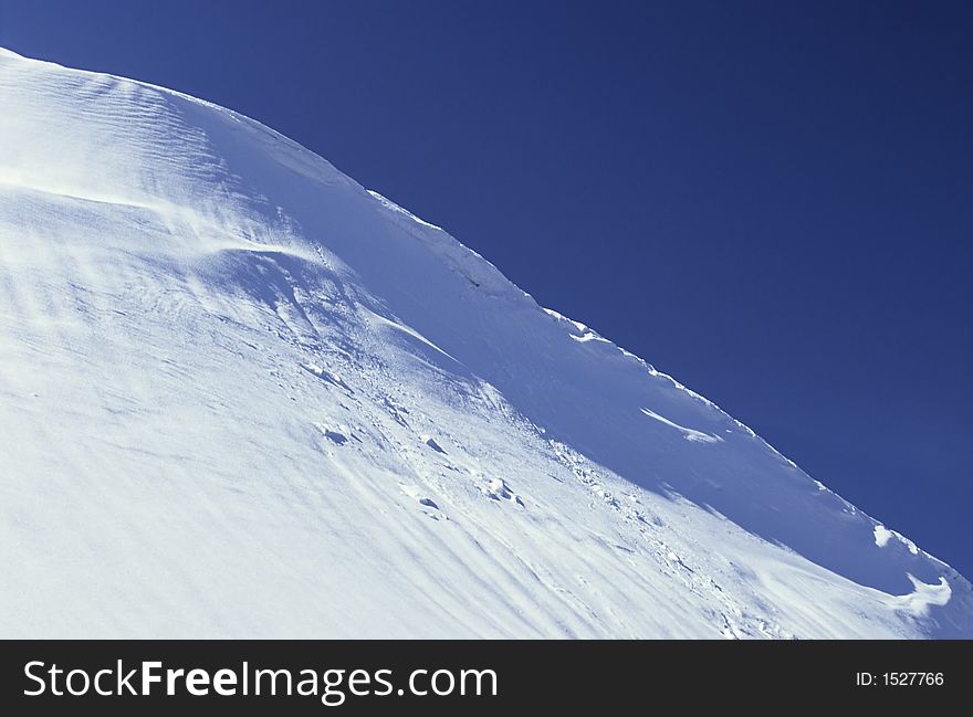 A ledge of snow on the top of a slope, blue and white symphony on a sunny day in winter. A ledge of snow on the top of a slope, blue and white symphony on a sunny day in winter