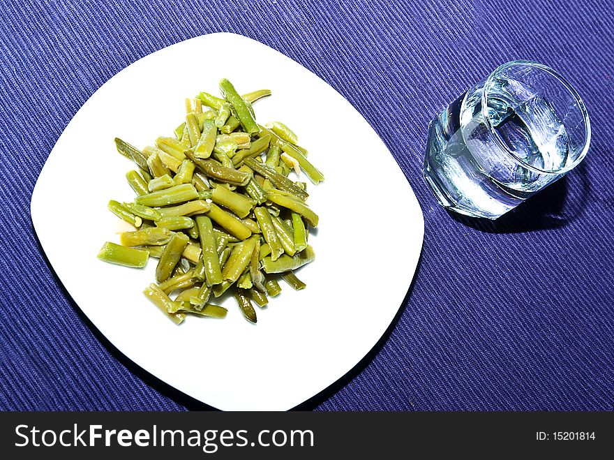 Presentation of green beans cooked on purple cloth with a glass of water