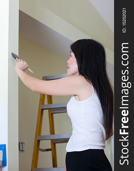 Asian Woman Contractor painting wall with ladder in background.