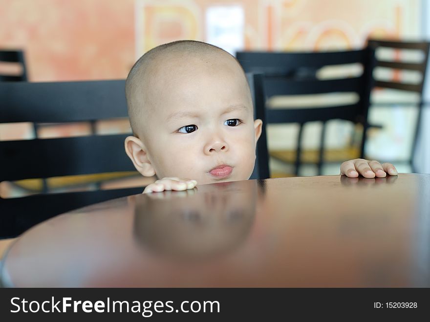 A Chinese boy is looking something and his hand holding the table.