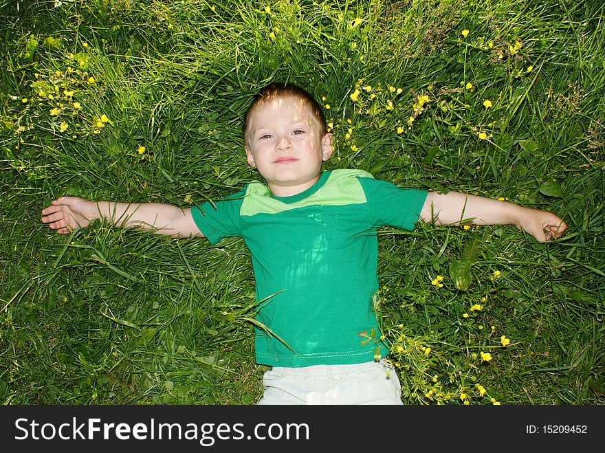 The boy lies in a meadow with outstretched arms, looking at the sky