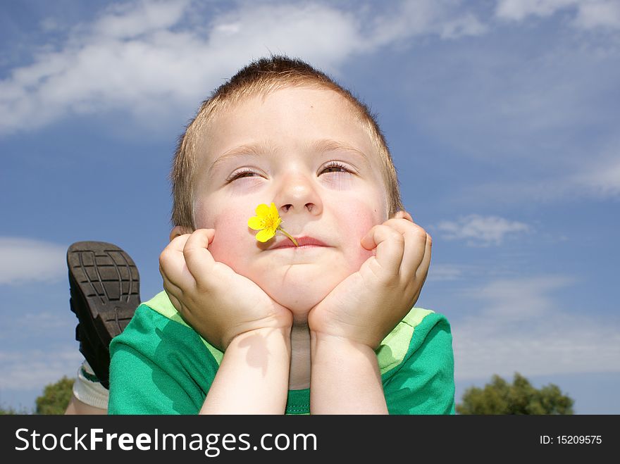 The boy lies in a meadow with flowers in the mouth