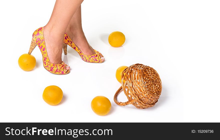 Woman feet in fashion shoes and oranges with basket isolated on white. Woman feet in fashion shoes and oranges with basket isolated on white