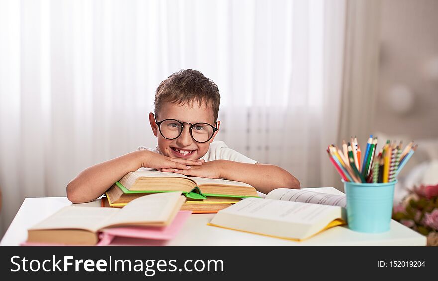 Joyful Little Boy Sitting At The Table With Pencils And Textbooks. Happy Child Pupil Doing Homework At The Table