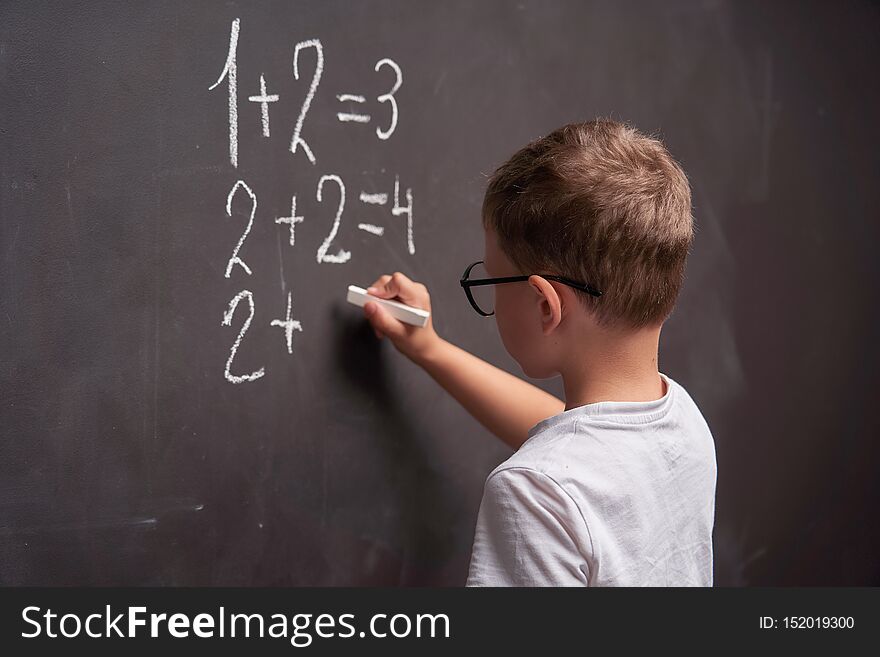 Rear view of a schoolboy solves a mathematical example on a blackboard in a math class