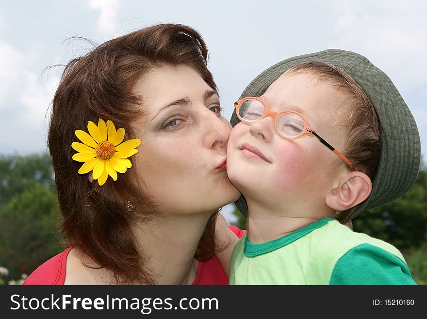 Young beautiful mother kissing her son,background nature