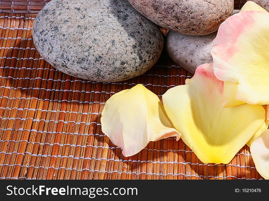 Yellow with a pink shade petals of roses on a wooden laying together with stones for salon SPA.