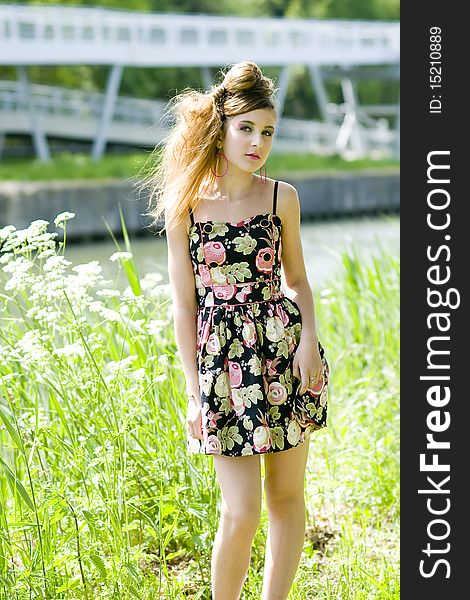 Teenager girl model presenting clothes in the park near the water and a bridge