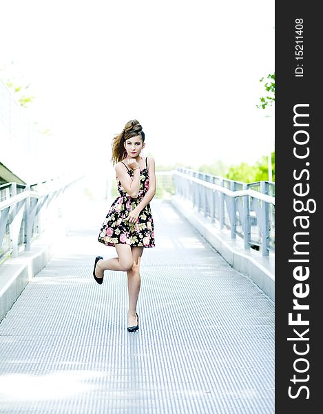 Teenager girl model presenting clothes on a bridge in the parc, light natural background