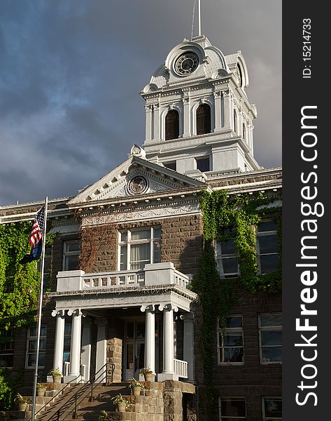 An American flag flies before the county courthouse in Prineville, Oregon, lit by the setting sun, against the background of a stormy sky. An American flag flies before the county courthouse in Prineville, Oregon, lit by the setting sun, against the background of a stormy sky