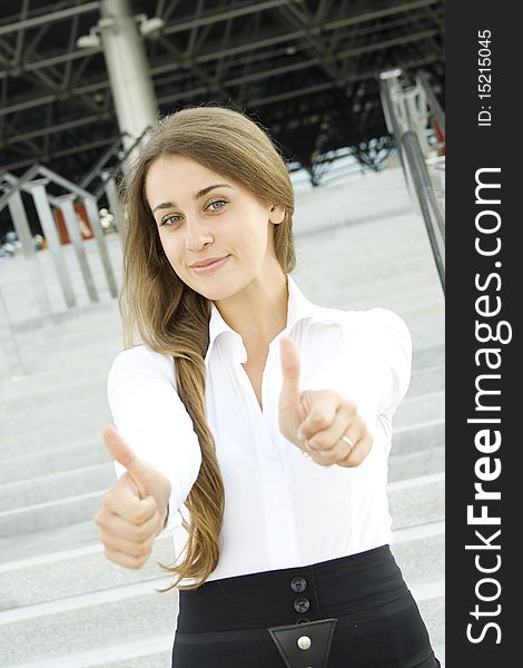 Young business woman on the background of an office building stairs thumbs up. Success. Joy. Young business woman on the background of an office building stairs thumbs up. Success. Joy.